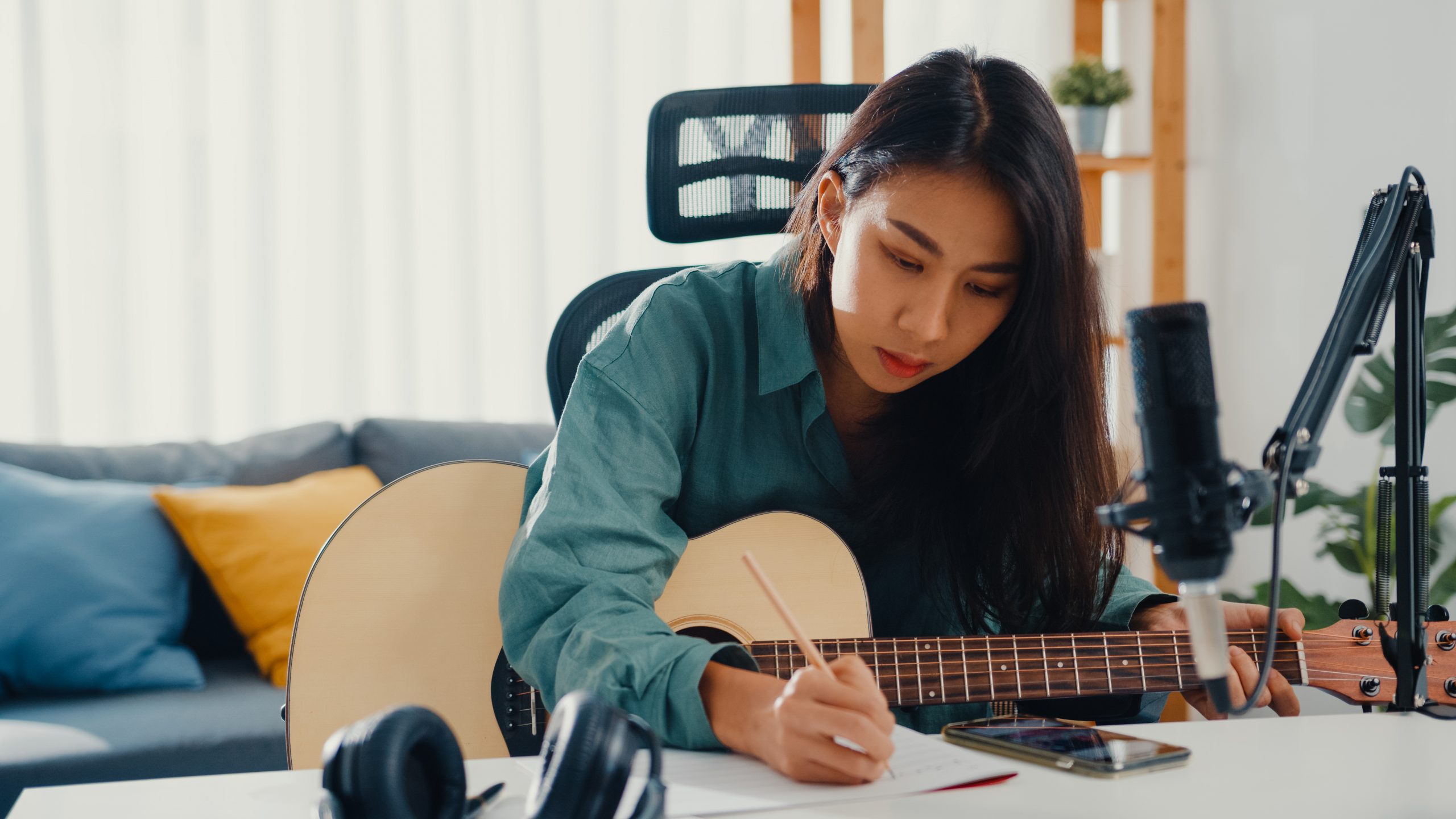 woman sitting in her living room writing on a score while holding a guitar