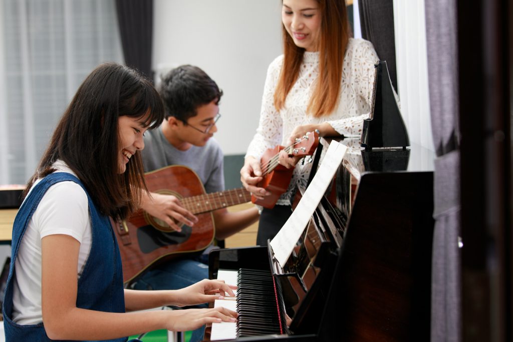 A group of adults playing piano in a living room during beginner lessons.