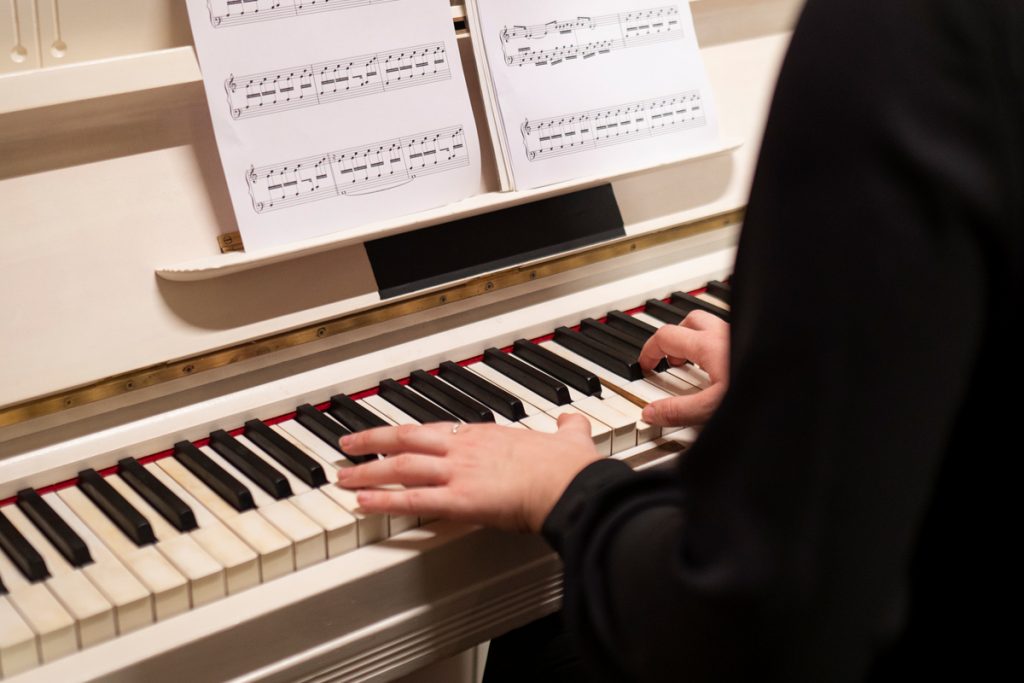 A person is playing a piano with music sheets in front of it during beginner piano lessons.