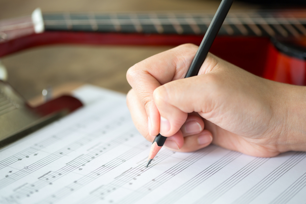 A person's hand is writing music notes on a sheet of paper, delving into the world of abrsm music theory.